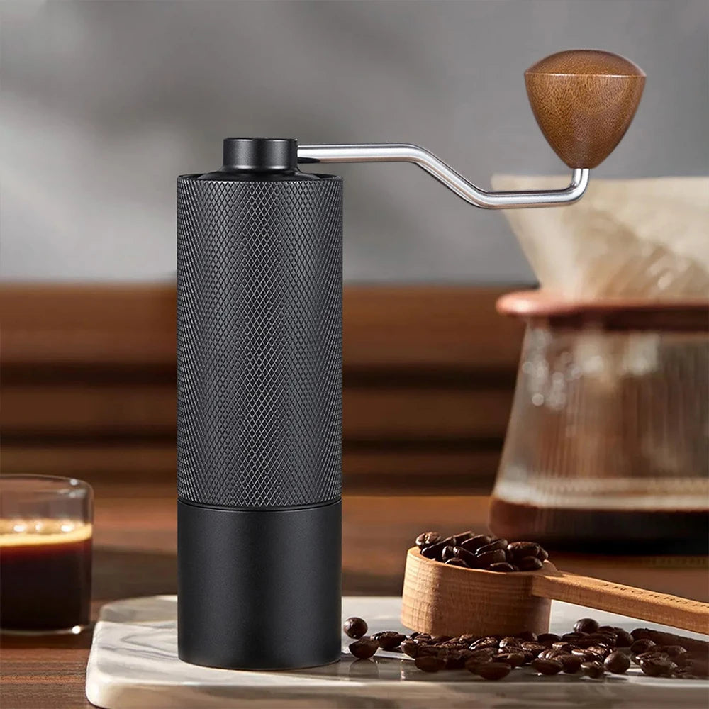 Moulin à café manuel noir avec pommeau en bois devant une cafetière filtre